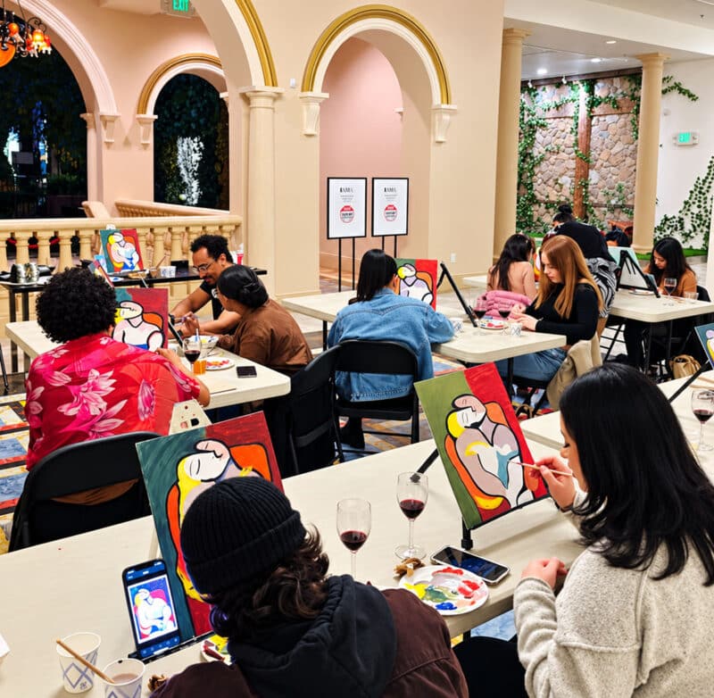 Guests participate in a painting workshop at the International Art Museum of America, seated around tables with easels as they create colorful abstract paintings.